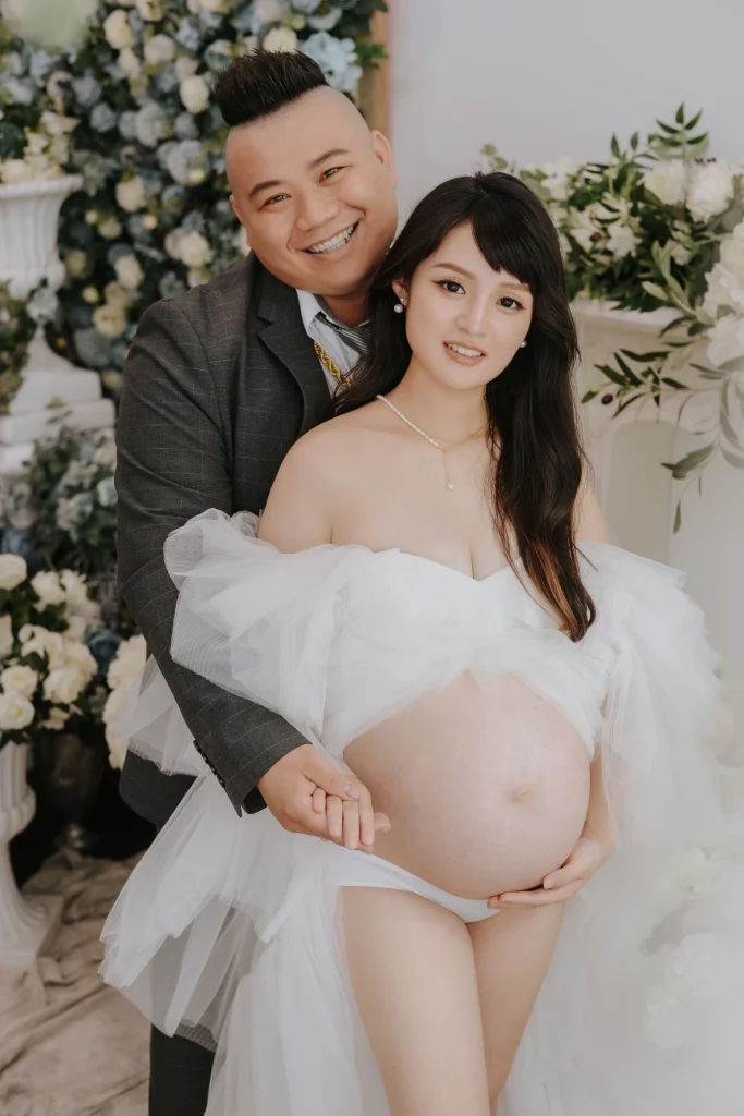 0000 0010 1 家庭寫真,夫妻在白色花藝背景前合照,芷妤穿白色薄紗展現孕肚