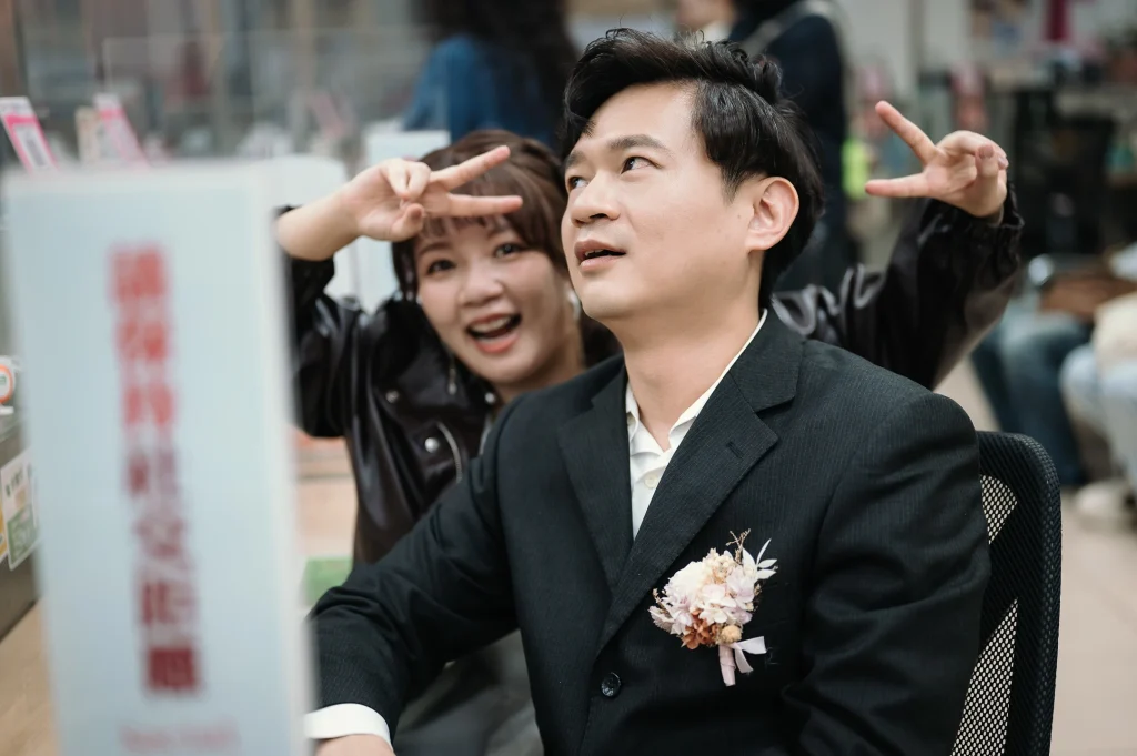 桃園婚攝作品，蔡先生在戶政辦公空間做出俏皮手勢，李小姐在後方微笑